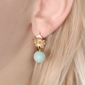 May include: Gold flower dangle earrings with a light blue round bead.