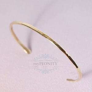 Pode incluir: Um bracelete de ouro martelado. O bracelete é simples e delicado, com um acabamento liso e polido.