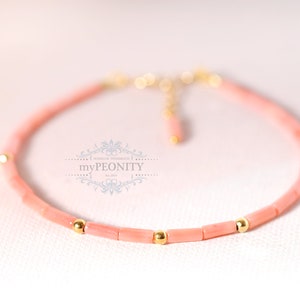 Può includere: Un delicato braccialetto di corallo rosa con perline dorate. Il braccialetto è realizzato con piccoli pezzi rettangolari di corallo e ha un design semplice ed elegante.