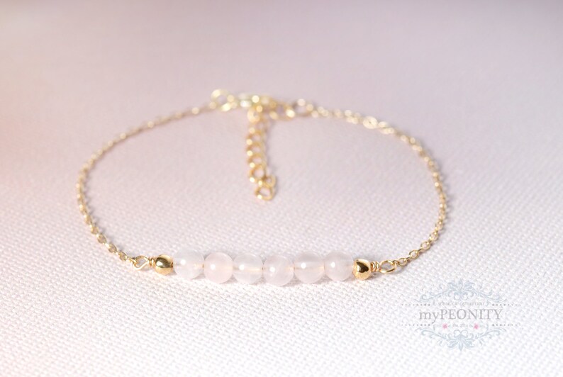 Puede incluir: Un delicado brazalete de cadena dorada con una fila de seis cuentas de color rosa p&aacute;lido. El brazalete tiene un cierre de mosquet&oacute;n.