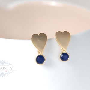 Könnte beinhalten: Goldene Ohrringe in Herzform mit einem blauen Edelstein, der daran hängt.