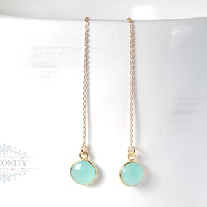 Może przedstawiać: Para złotych kolczyków z łańcuszkiem i niebieskimi kamieniami.