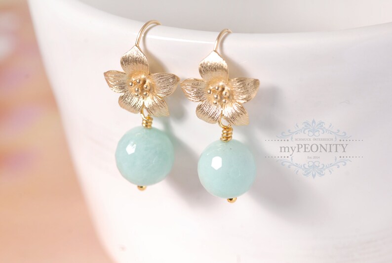May include: Gold flower dangle earrings with light blue round gemstone drops.