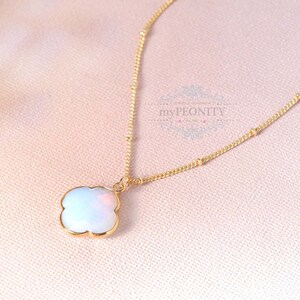 Könnte beinhalten: Eine goldene Kettenkette mit einem weißen Opal-Kleeblatt-Anhänger. Die Kette hat kleine goldene Perlen.