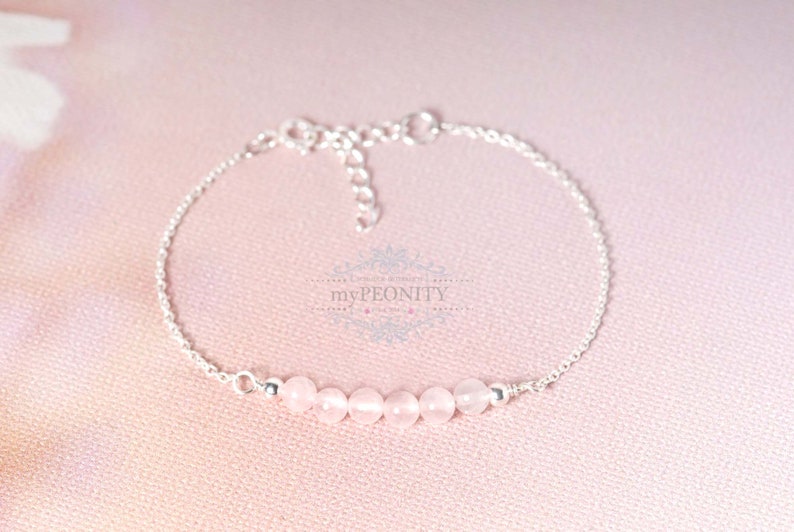 Puede incluir: Un delicado brazalete de cadena de plata con una fila de seis cuentas de piedras preciosas de color rosa p&aacute;lido.