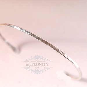 Peut inclure: Un bracelet jonc en argent martelé. Le bracelet est fin et délicat, avec une finition lisse et polie.