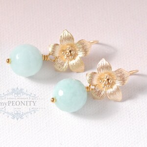 May include: A pair of gold earrings with a light blue round gemstone and a gold flower charm.