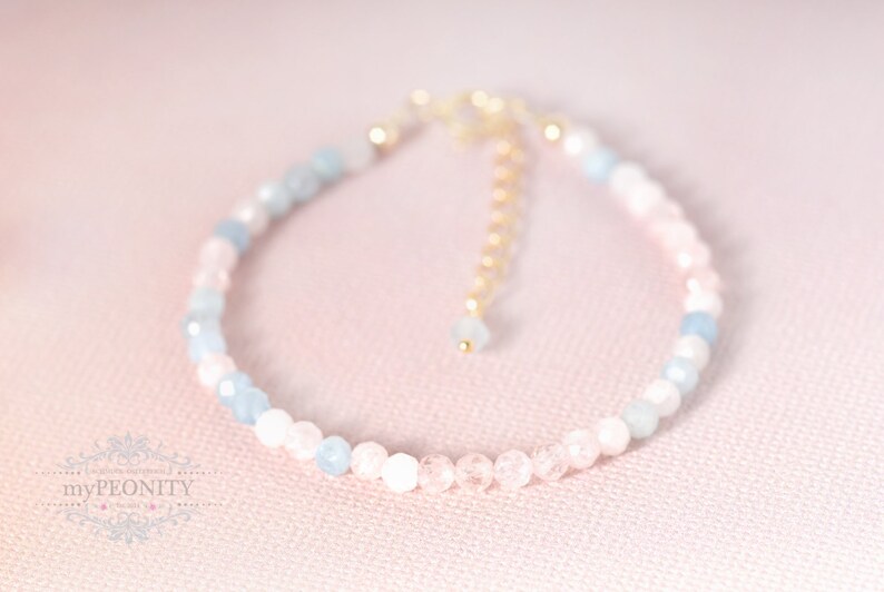 May include: A delicate bracelet made with light blue and pink beads, accented with a gold chain clasp.