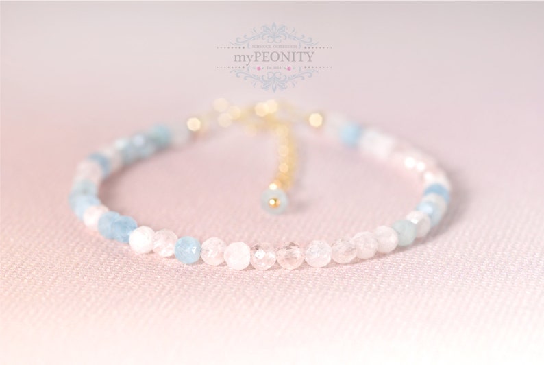 May include: A delicate bracelet made with light blue and white beads. The bracelet has a gold clasp and is adjustable.