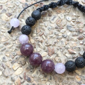 Puede incluir: Un brazalete de cordón negro con cuentas de piedras preciosas moradas y rosadas y cuentas de roca volcánica negra.