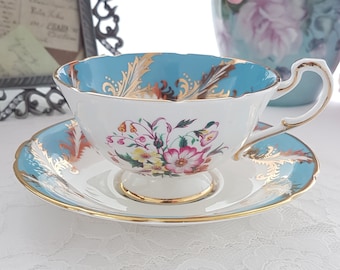 May include: A vintage teacup and saucer set with a blue and white floral pattern and gold accents. The cup and saucer have a scalloped edge.