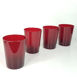 May include: Set of four red glass tumblers. The glasses are clear with a red tint and have a rounded bottom.