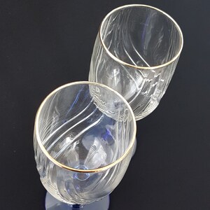 May include: Two clear glass wine glasses with gold rims. The glasses have a textured, wavy design.