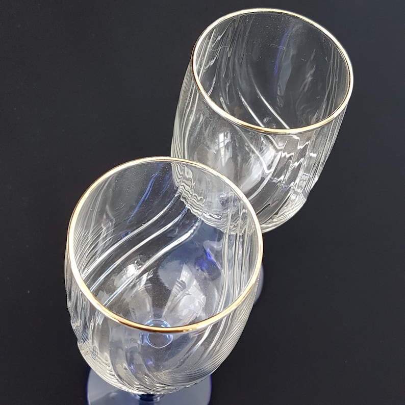 May include: Two clear glass wine glasses with gold rims. The glasses have a textured, wavy design.
