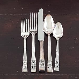 May include: A set of five silver-plated flatware pieces, including a knife, fork, and three spoons. The pieces have ornate floral designs on the handles.