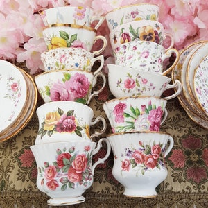 May include: A collection of vintage teacups and saucers, featuring floral patterns in pink, yellow, and red. The teacups have gold trim and are arranged on a patterned surface, with pink flowers in the background. A classic tea party theme.