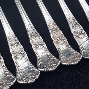 Puede incluir: Seis tenedores de plata con mangos ornamentados. Los mangos están decorados con un diseño floral y tienen un monograma.