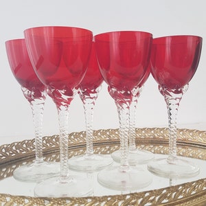 May include: Set of six red glass wine glasses with twisted stems. The glasses are arranged on a gold tray.