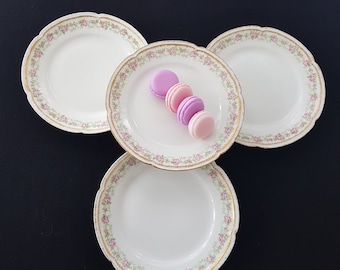 May include: Three white porcelain plates with gold trim and a floral design. The plates are arranged in a triangle shape with a stack of four pink and purple macarons on the center plate.