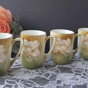 May include: Set of four vintage porcelain mugs with a floral design. Each mug features a white carnation with green leaves on a yellow background.