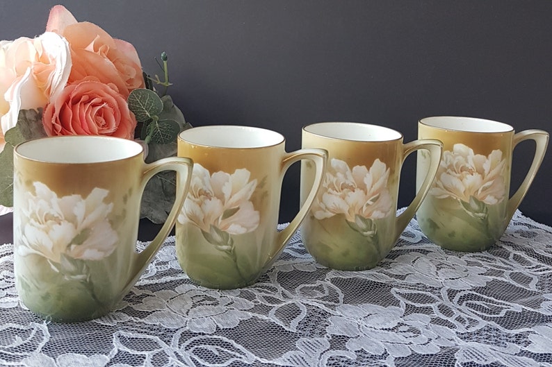 May include: Set of four vintage porcelain mugs with a floral design. Each mug features a white carnation with green leaves on a yellow background.