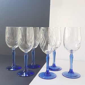May include: Six clear glass wine glasses with blue stems. The glasses are arranged in a row on a white surface.