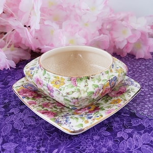 May include: A square, floral patterned ceramic dish with a matching, smaller bowl. The dish and bowl have a gold trim around the edges.