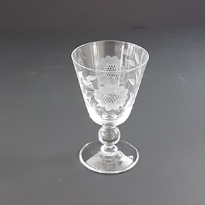 May include: A clear glass goblet with an etched floral pattern. The goblet features a round base, a spherical stem, and a flared bowl. The floral design includes flowers and leaves. The goblet is suitable for serving wine or other drinks.