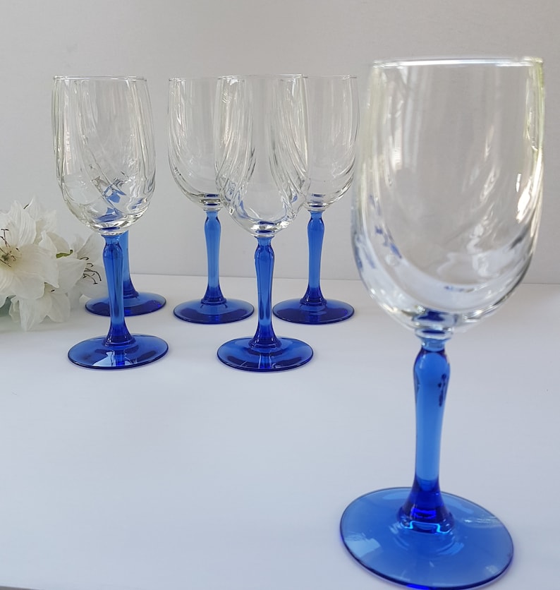 May include: Set of six clear glass wine glasses with blue stems. The glasses have a swirl design and are perfect for serving wine.