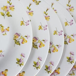 May include: Set of five white ceramic dinner plates with a floral pattern of purple and yellow flowers.