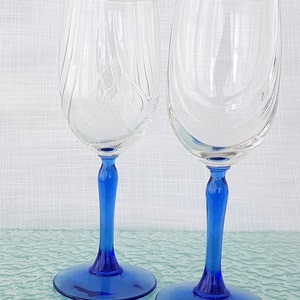 May include: Two clear glass wine glasses with blue stems and bases. The glasses are empty and sitting on a blue surface.