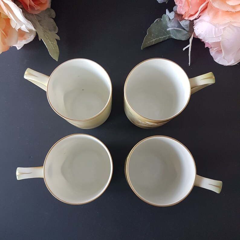 May include: Set of four white porcelain teacups with gold trim. The cups have a floral design on the outside.