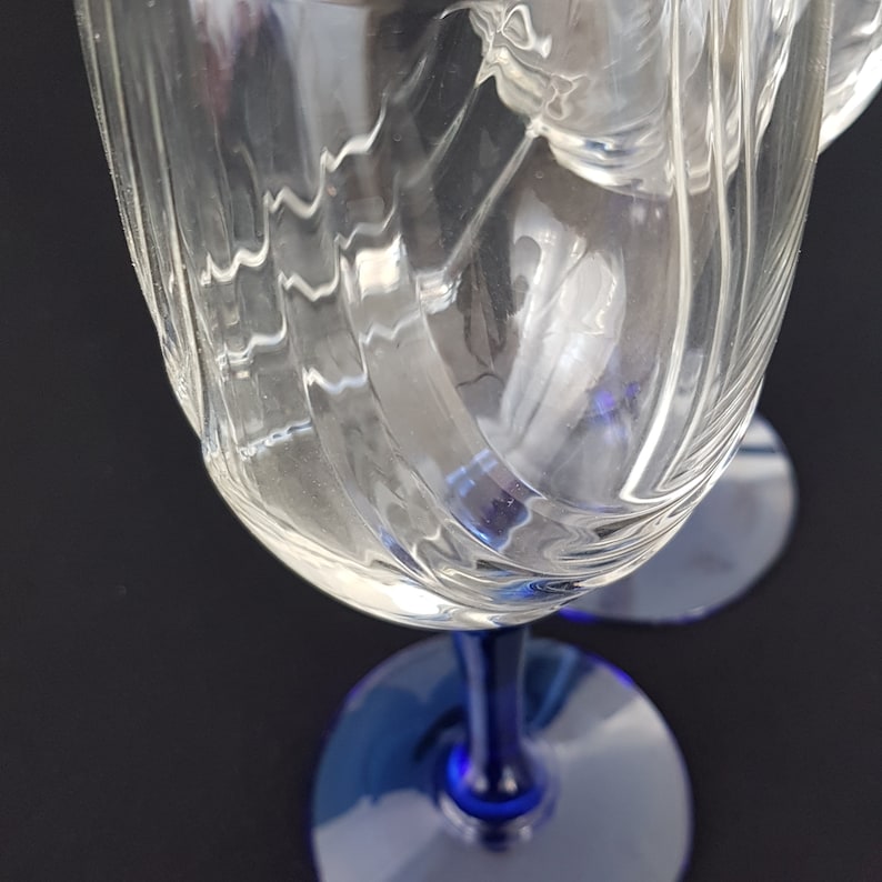 May include: Two clear glass wine glasses with a blue stem and base. The glasses have a swirl design.