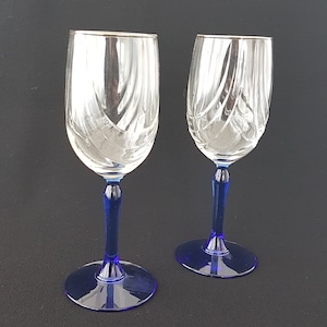 May include: Two clear glass wine glasses with blue stems and silver rims. The glasses have a swirl pattern.