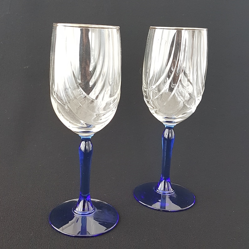 May include: Two clear glass wine glasses with blue stems and silver rims. The glasses have a swirl pattern.