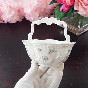 May include: White porcelain basket with a handle, decorated with blue floral patterns and embossed scrollwork. The rim and handle have intricate detailing. A decorative piece for serving or display.