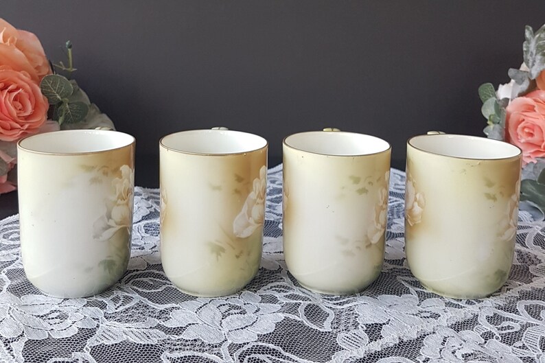 May include: Four white porcelain mugs with a floral design. The mugs have a light green and brown background with white flowers. The mugs are all the same size and shape.