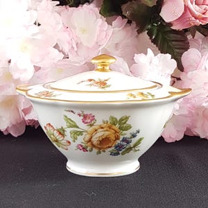 Peut inclure: Un sucrier en porcelaine blanche avec un couvercle, orné d'un motif floral avec des fleurs jaunes, roses et bleues. Le bol a une bordure dorée et un bouton doré sur le couvercle.