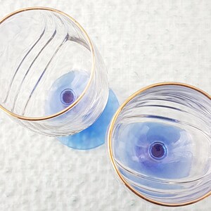 May include: Two clear glass wine glasses with a gold rim and a blue base. The glasses have a textured design.