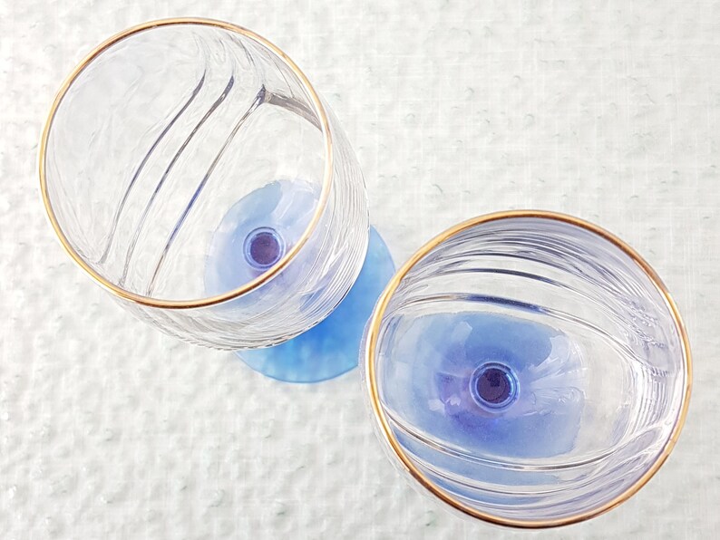 May include: Two clear glass wine glasses with a gold rim and a blue base. The glasses have a textured design.