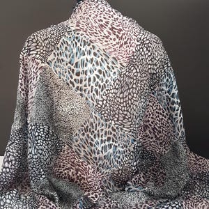 Peut inclure: Un tissu à motifs avec des taches et des formes noires, blanches, grises et marron, avec des touches de bleu clair. Le tissu est drapé, révélant sa texture et son tombé.