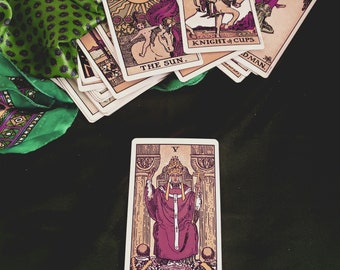 May include: A tarot card reading with a green and purple patterned fabric in the background. The cards are spread out on the fabric, and the card in the foreground is "The Hierophant".