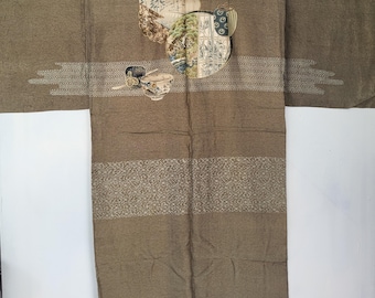 May include: A brown kimono with embroidered details. The garment features decorative panels with landscape and floral designs, along with horizontal bands of patterned fabric. The kimono is displayed against a white background.