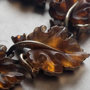 May include: A bracelet featuring translucent amber-colored carved leaf-shaped components linked together with silver-toned metal. Each leaf segment is accented with a small, round, amber-colored faceted stone set in a silver-toned metal frame.