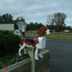 May include: A white mailbox with a black and brown beagle dog design. The mailbox is mounted on a wooden post.