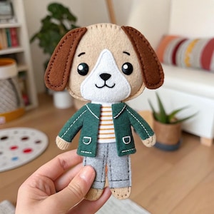 Può includere: Una bambola a forma di cane in feltro fatta a mano con testa beige, orecchie marroni e muso bianco. Il cane indossa una giacca verde sopra una camicia a righe e pantaloni grigi. La bambola ha occhi neri e naso e bocca neri cuciti.