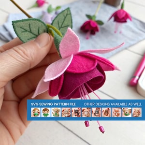 Puede incluir: Una flor de fucsia de fieltro hecha a mano con pétalos superpuestos de color rosa claro y magenta intenso, hojas verdes y estambres finos. Una banda azul en la parte inferior muestra el texto SVG SEWING PATTERN FILE OTHER DESIGNS AVAILABLE AS WELL.