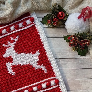 May include: A red and white crocheted Christmas stocking with a white reindeer design and white pom-poms around the edges.