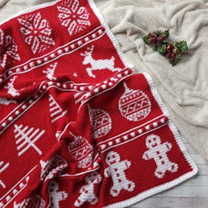 May include: A red crochet blanket with white Christmas-themed motifs, including snowflakes, reindeer, Christmas trees, ornaments, and gingerbread men.