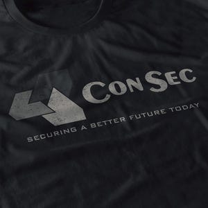 Peut inclure: T-shirt noir avec le texte "Con Sec" en lettres blanches usées. En dessous, la phrase "Securing a Better Future Today" dans une police assortie. Le t-shirt présente un logo géométrique sur le côté gauche.